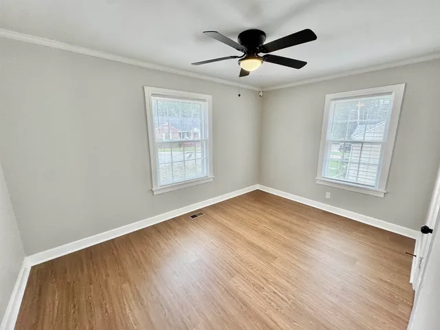 an empty room with wooden floor chandelier fan and windows