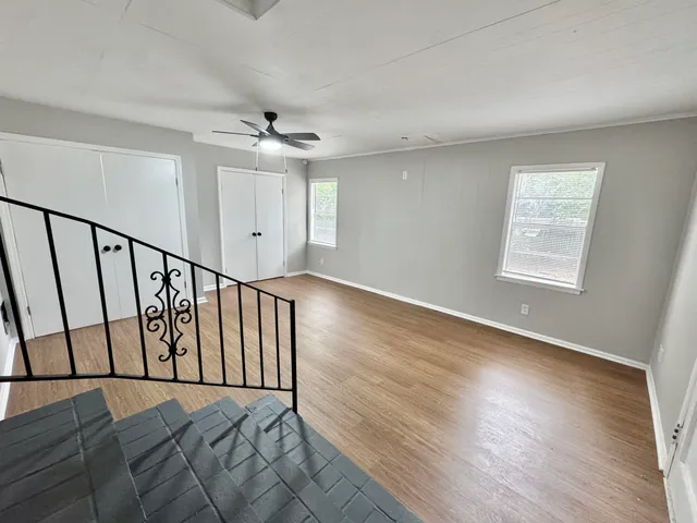 an empty room with wooden floor fan and windows
