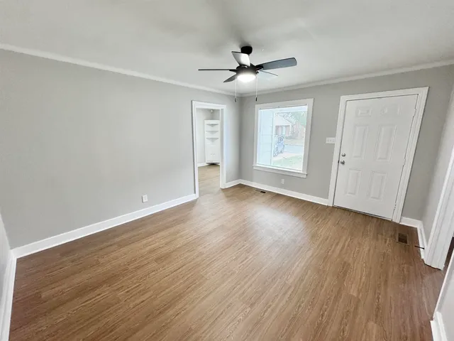 a view of an empty room with wooden floor and a ceiling fan