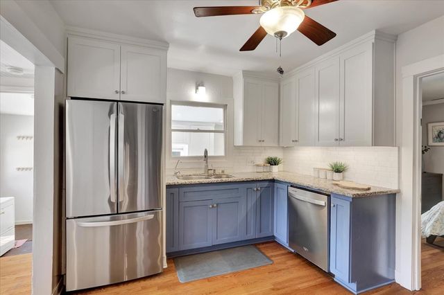 a kitchen with stainless steel appliances kitchen island granite countertop a refrigerator a sink dishwasher a dining table and chairs with wooden floor
