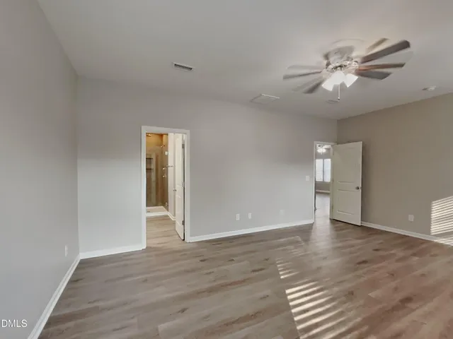 a view of an empty room with wooden floor and a ceiling fan