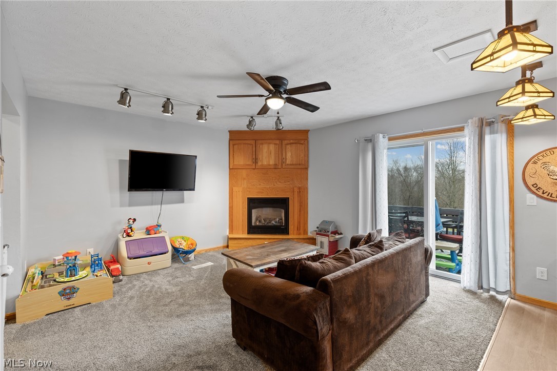 64508 Slade Road Cambridge, OH 43725 - Photo 16 of 50 Carpeted family room with track lighting, a large fireplace, a ceiling fan, and a textured ceiling
