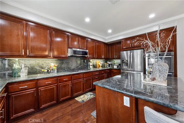 a kitchen with stainless steel appliances granite countertop a refrigerator a stove and a sink with wooden floors