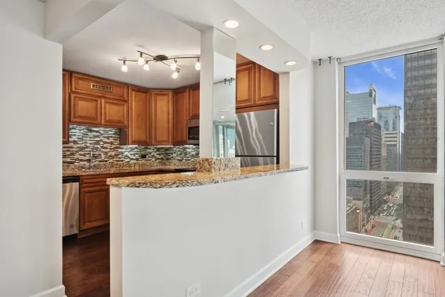 a kitchen with stainless steel appliances granite countertop a refrigerator a sink dishwasher a stove and white countertops with wooden floor