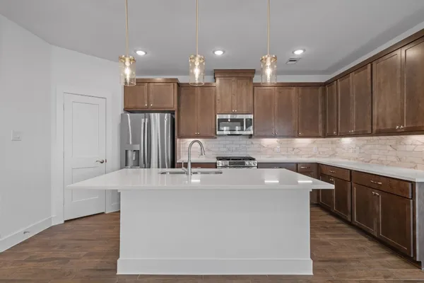 a kitchen with stainless steel appliances granite countertop a sink a stove a refrigerator and island with wooden floor