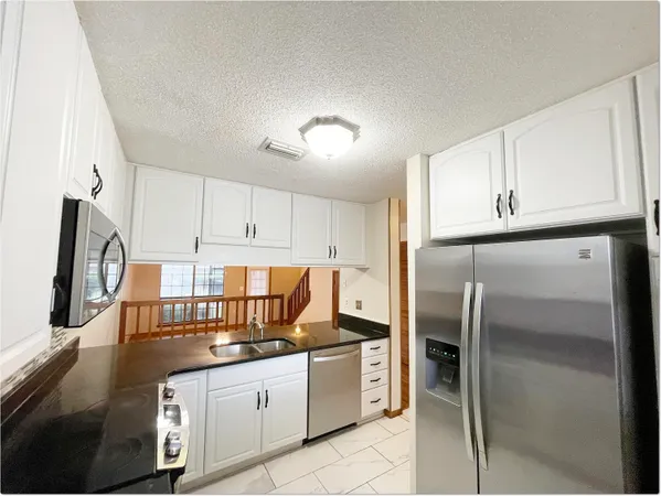 a kitchen with granite countertop a refrigerator stove and white cabinets