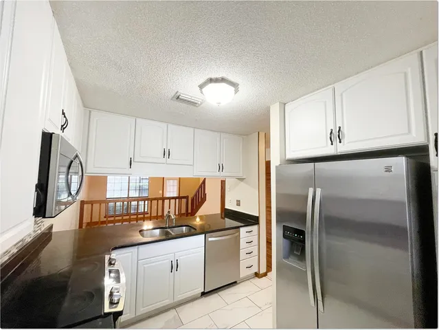 a kitchen with granite countertop a refrigerator stove and white cabinets