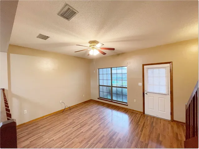 an empty room with wooden floor chandelier fan and windows