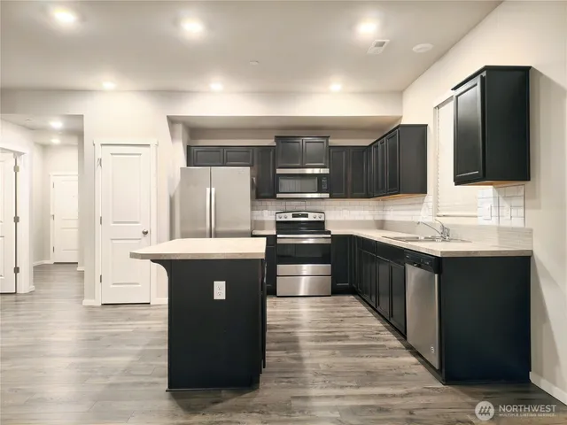 a large kitchen with stainless steel appliances kitchen island granite countertop a stove a sink dishwasher and a refrigerator with wooden floor