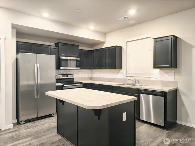 a kitchen with stainless steel appliances a refrigerator a sink a stove a microwave and wooden cabinets