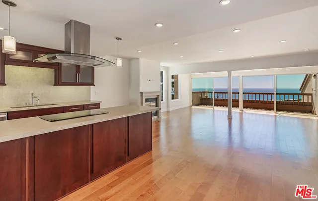 a open kitchen with stainless steel appliances a large counter top a stove and a wooden floors