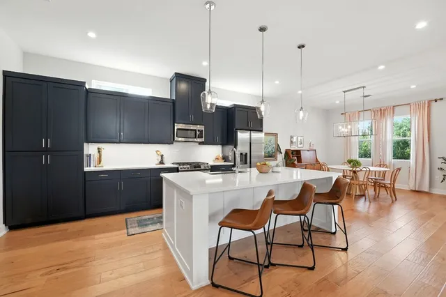 a kitchen with stainless steel appliances kitchen island granite countertop a refrigerator a stove top oven and a dining table with wooden floor