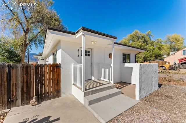 a view of a white house with a small yard and wooden fence