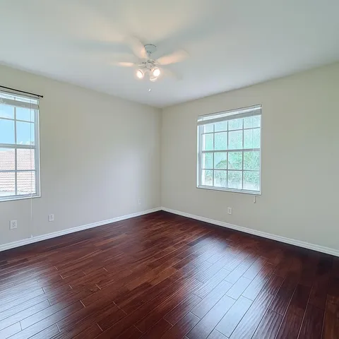 an empty room with wooden floor chandelier fan and windows