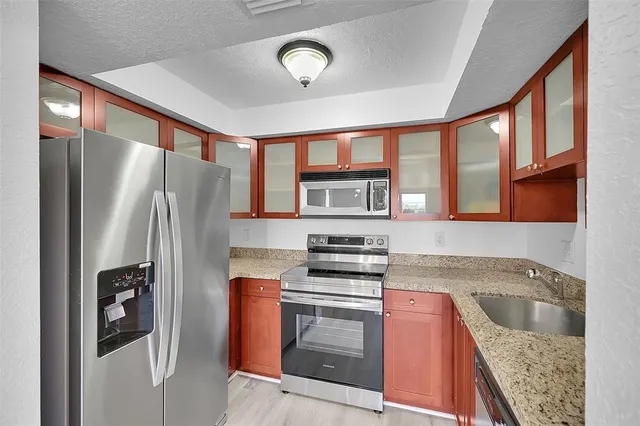 a kitchen with stainless steel appliances granite countertop a refrigerator a stove and a sink with large window