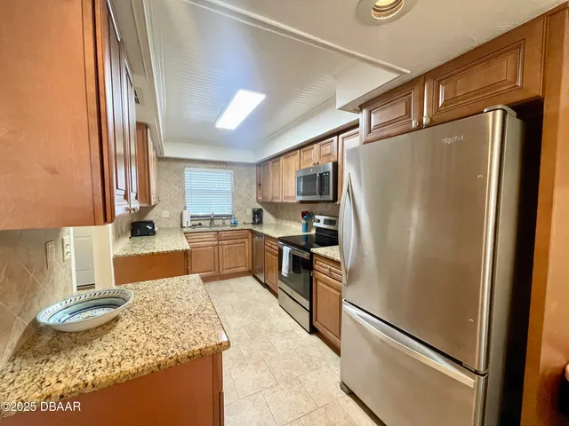 a kitchen with granite countertop stainless steel appliances a refrigerator a stove top oven and sink