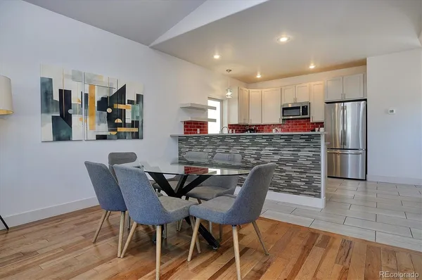 a kitchen with stainless steel appliances kitchen island granite countertop a dining table chairs and a refrigerator