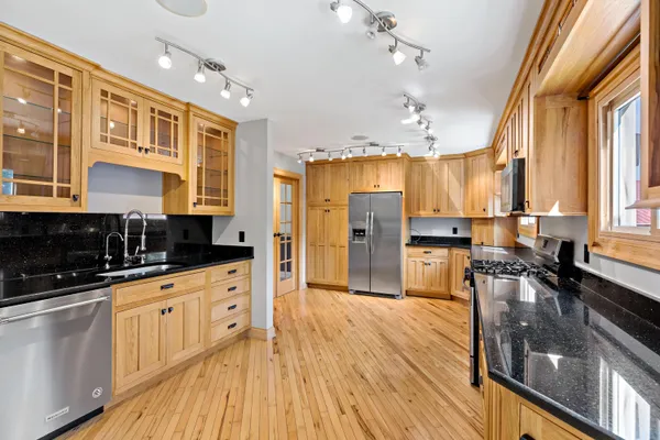 a kitchen with granite countertop a refrigerator a sink dishwasher a stove and white cabinets with wooden floor