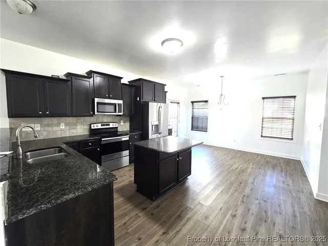 a kitchen with stainless steel appliances granite countertop a refrigerator a stove top oven a sink dishwasher and wooden cabinets with wooden floor