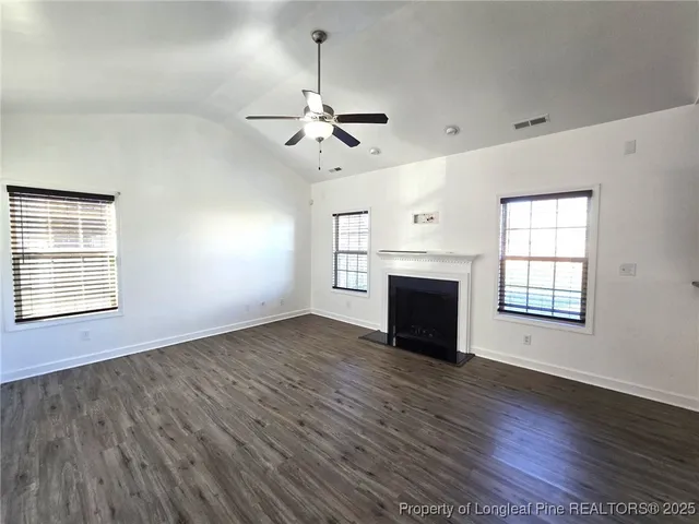 a view of an empty room with wooden floor fireplace and a window