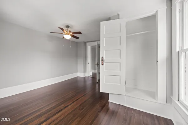 an empty room with wooden floor chandelier fan and windows