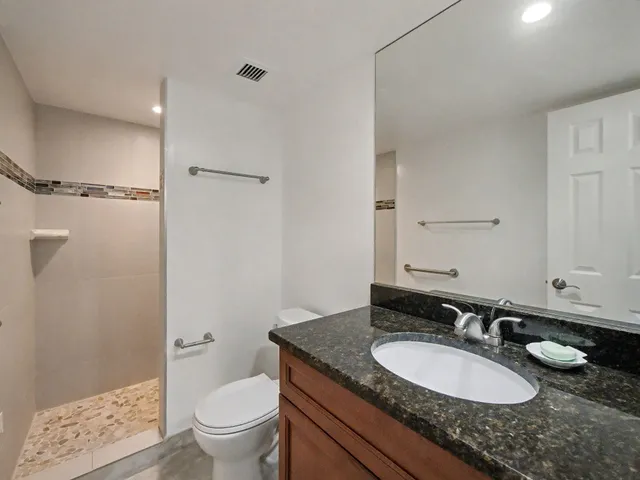 a bathroom with a granite countertop sink a toilet a mirror and shower