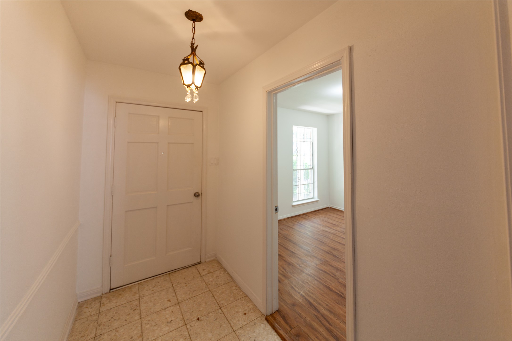 8826 Roos Road Houston, TX 77036 - Photo 2 of 42 Bright entryway with tile flooring and a classic light fixture. Leads into a room with wood flooring and a large window.