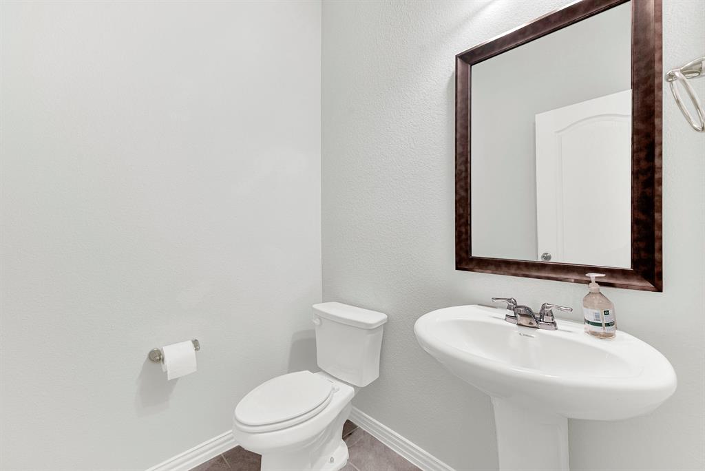 7640 Rhyner Way Fort Worth, TX 76137 - Photo 7 of 40 Elegant powder room featuring a pedestal sink with chrome faucet, white porcelain toilet, and a wood-framed mirror above marble countertops