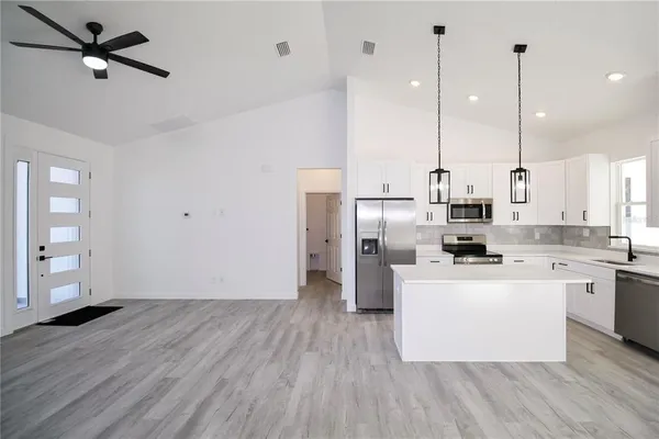 a kitchen with stainless steel appliances a stove top oven a sink a refrigerator a center island and wooden floor