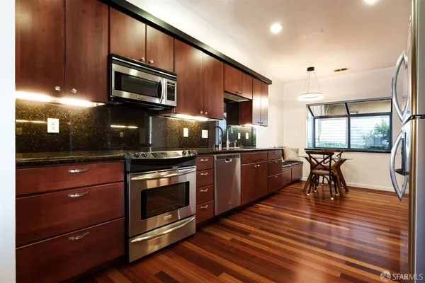 a kitchen with stainless steel appliances granite countertop a refrigerator a stove and a wooden floors
