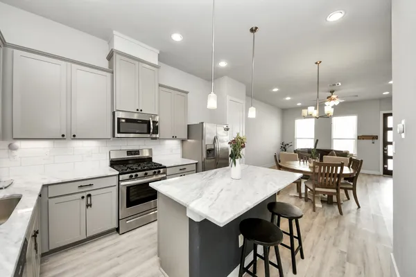 a kitchen with stainless steel appliances kitchen island granite countertop a stove a sink a microwave a dining table and chairs with wooden floor