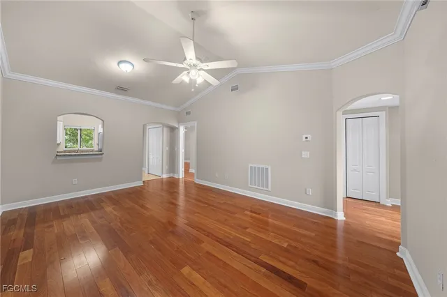 an empty room with wooden floor chandelier fan and windows