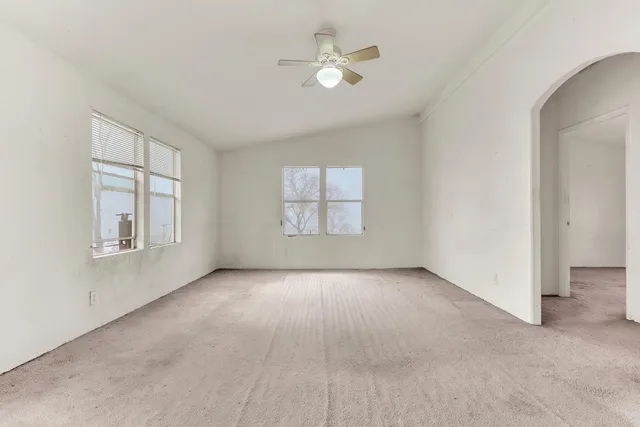 an empty room with chandelier fan and windows