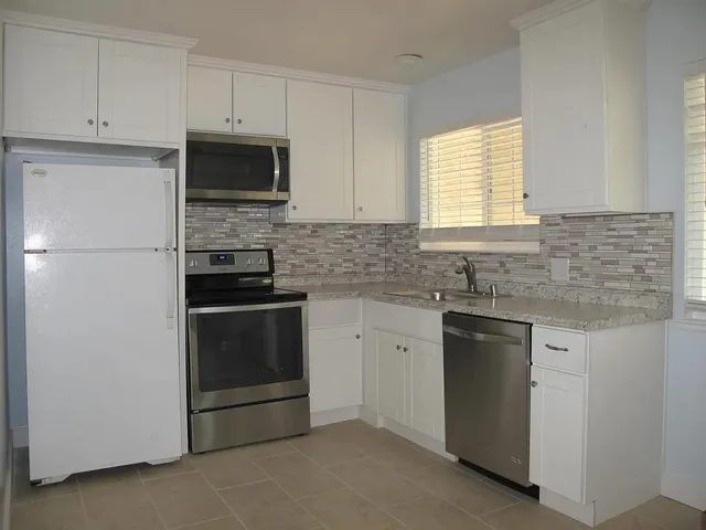 a kitchen with granite countertop white cabinets stainless steel appliances and a window