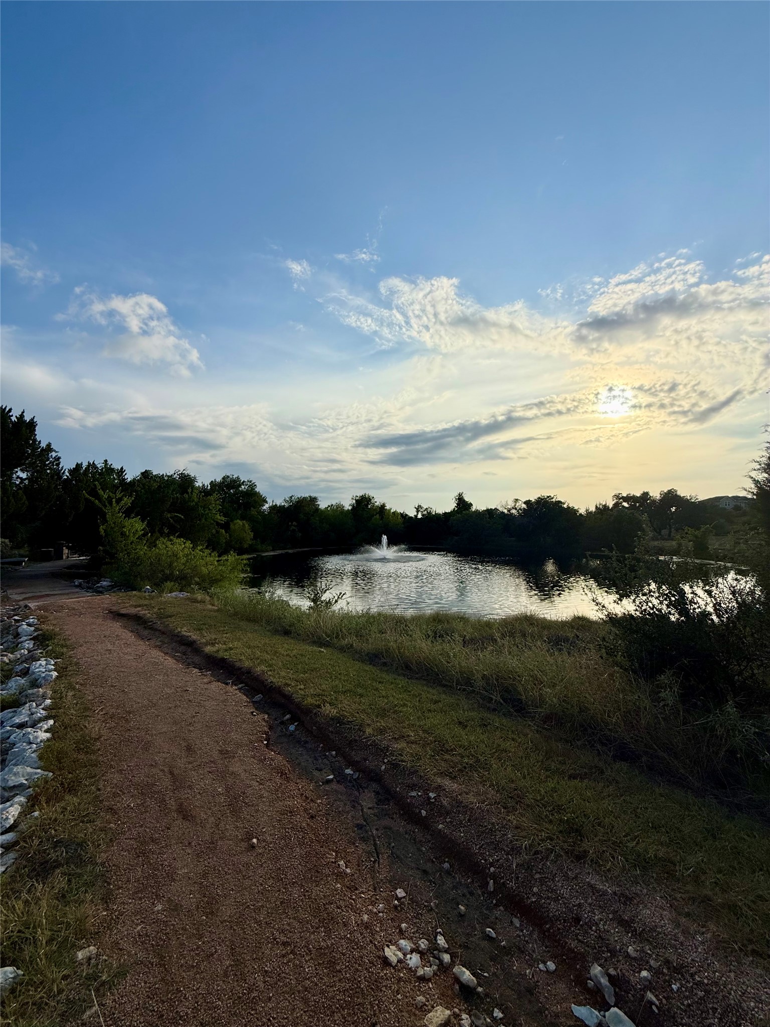 105 Merrick Road Georgetown, TX 78628 - Photo 21 of 23 Scenic pond with a serene fountain, nestled beside a walking path under a vast, open sky.