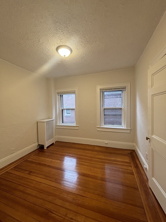 6 Beals Street, Unit 2 Brookline, MA 02446 - Photo 5 of 9 an empty room with wooden floor and windows