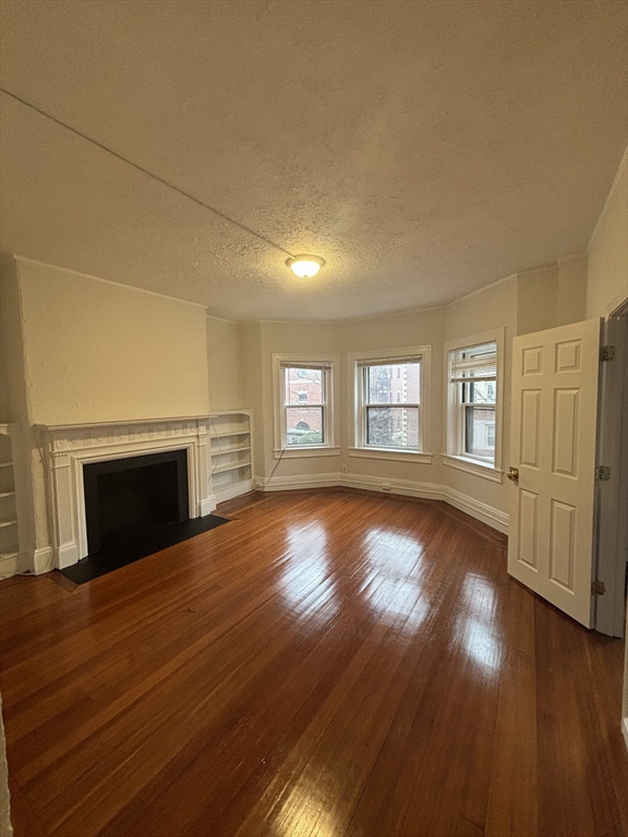 6 Beals Street, Unit 2 Brookline, MA 02446 - Photo 8 of 9 a view of empty room with wooden floor and fireplace