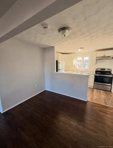 an empty room with wooden floor and kitchen view