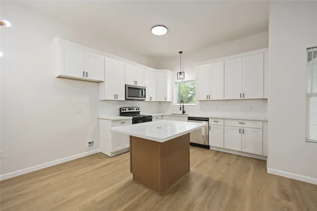 a kitchen with cabinets appliances wooden floor and a window