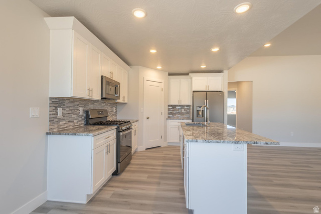 910 East Remington Road Cedar City, UT 84721 - Photo 6 of 29 Modern kitchen featuring white cabinetry, a large center island with a stone countertop, stainless steel appliances, and wood-finish flooring