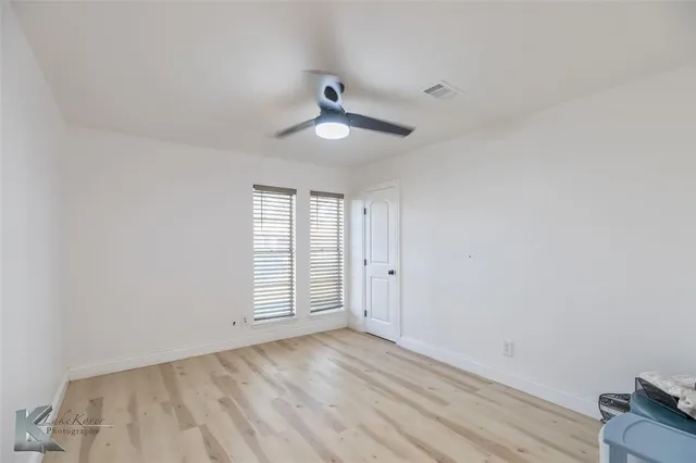 an empty room with wooden floor ceiling fan and windows