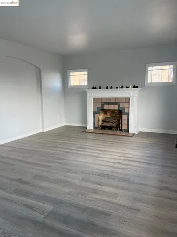 a view of an empty room with wooden floor fireplace and a window