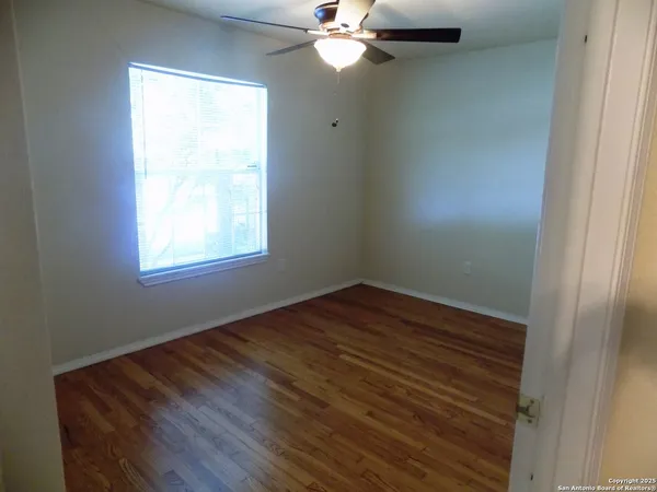 an empty room with wooden floor windows and fan