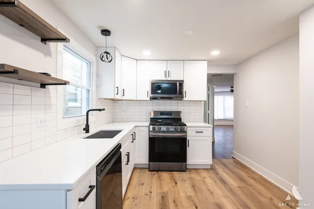 a kitchen with stainless steel appliances a refrigerator a sink dishwasher a stove and white countertops with wooden floor