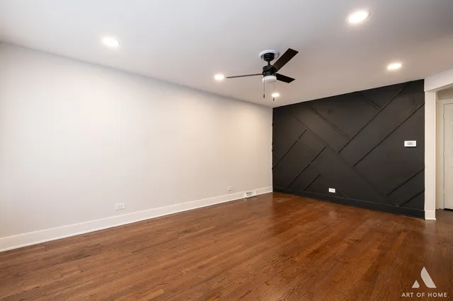 a view of an empty room with wooden floor and a ceiling fan