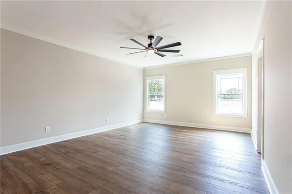 an empty room with wooden floor ceiling fan and windows