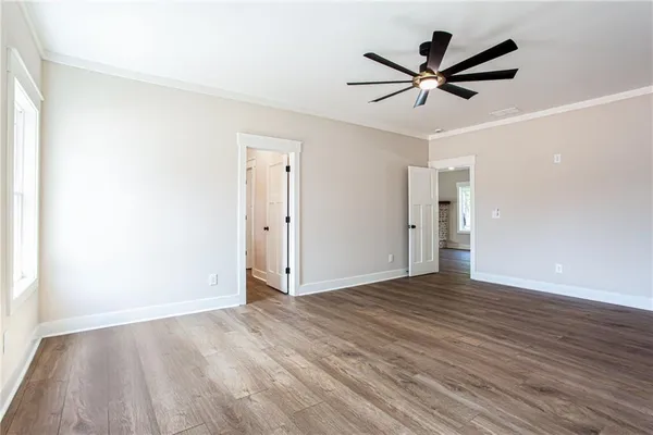 a view of an empty room with wooden floor and a ceiling fan