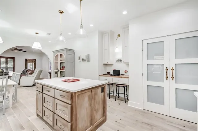 a open kitchen with kitchen island a stove a sink a refrigerator and white cabinets with wooden floor