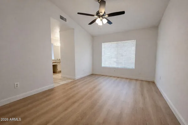 an empty room with wooden floor chandelier fan and windows