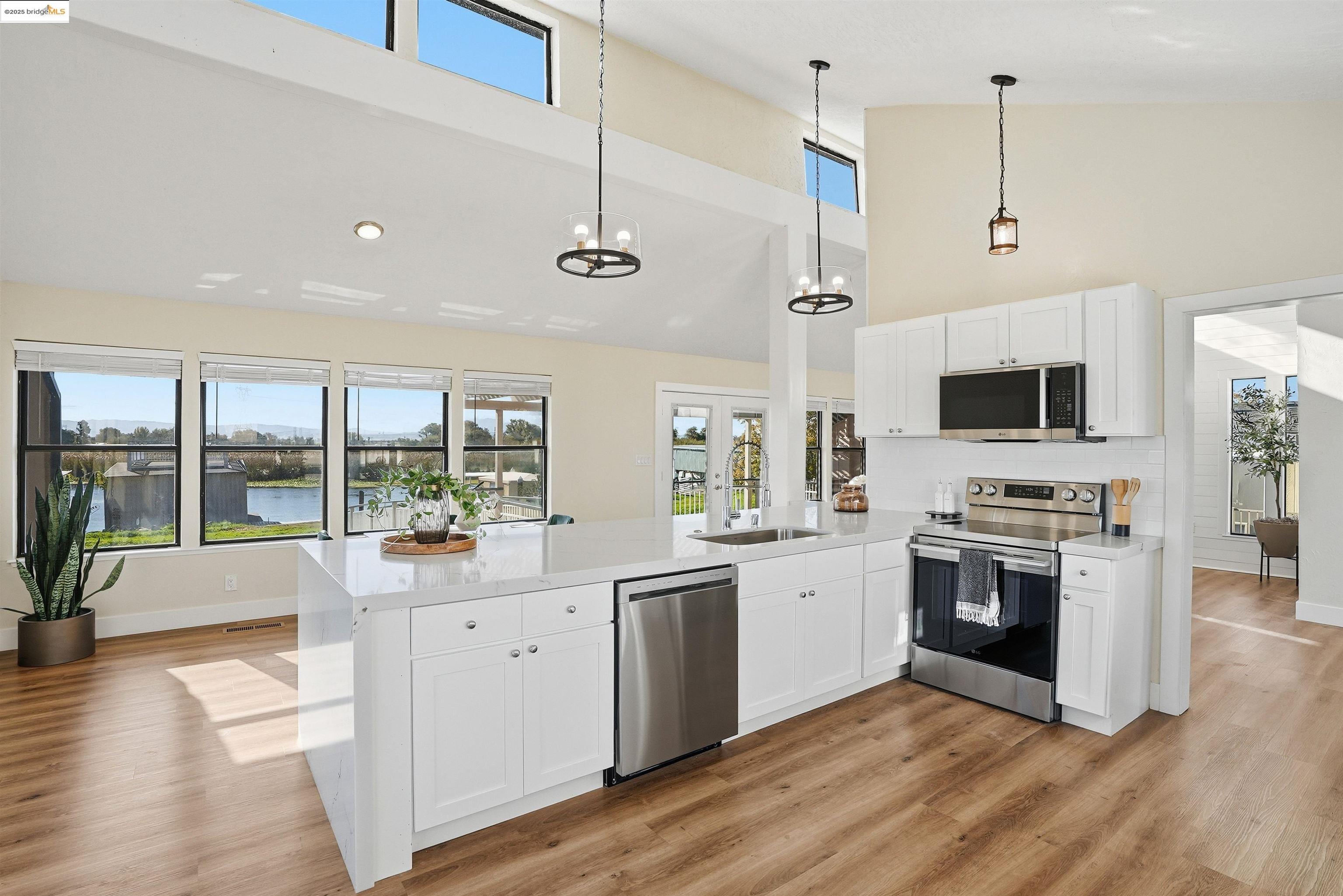 2796 Taylor Road Bethel Island, CA 94511 - Photo 11 of 49 Kitchen featuring stainless steel appliances, healthy amount of natural light, white cabinetry, light stone countertops, and a high ceiling